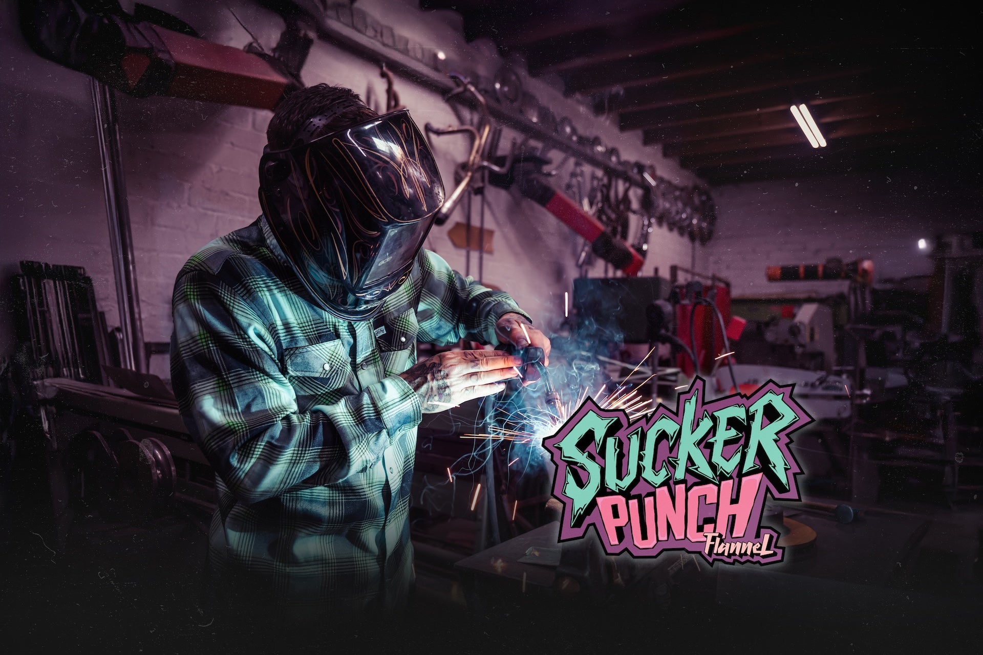 Person welding with a darkened helmet in a workshop, featuring 'Sucker Punch' graphic.