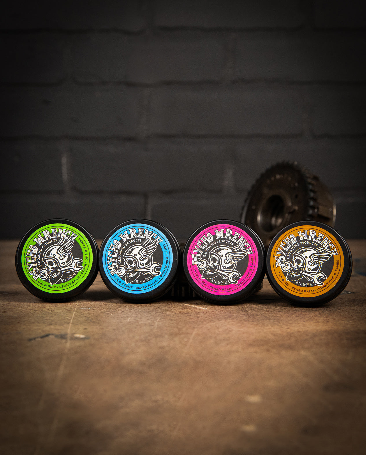 Four circular products with colorful labels on a wooden surface and dark brick wall background - Beard Balm Variety 4-pack by greasy hands society