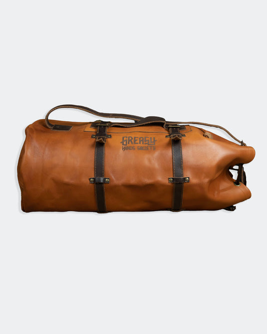 Brown leather duffel bag with dark brown straps on a gray background from greasy hands society