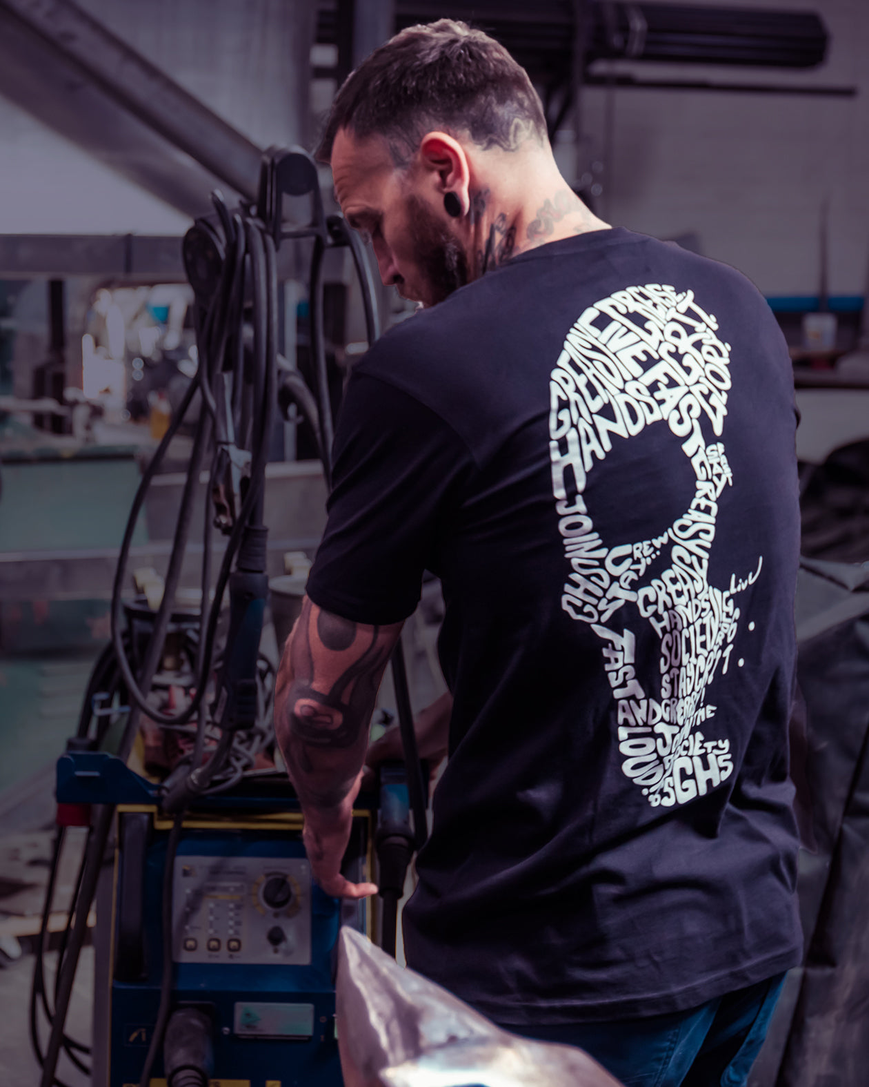 Person wearing a black t-shirt with a white skull graphic design, working on a car in a shop
