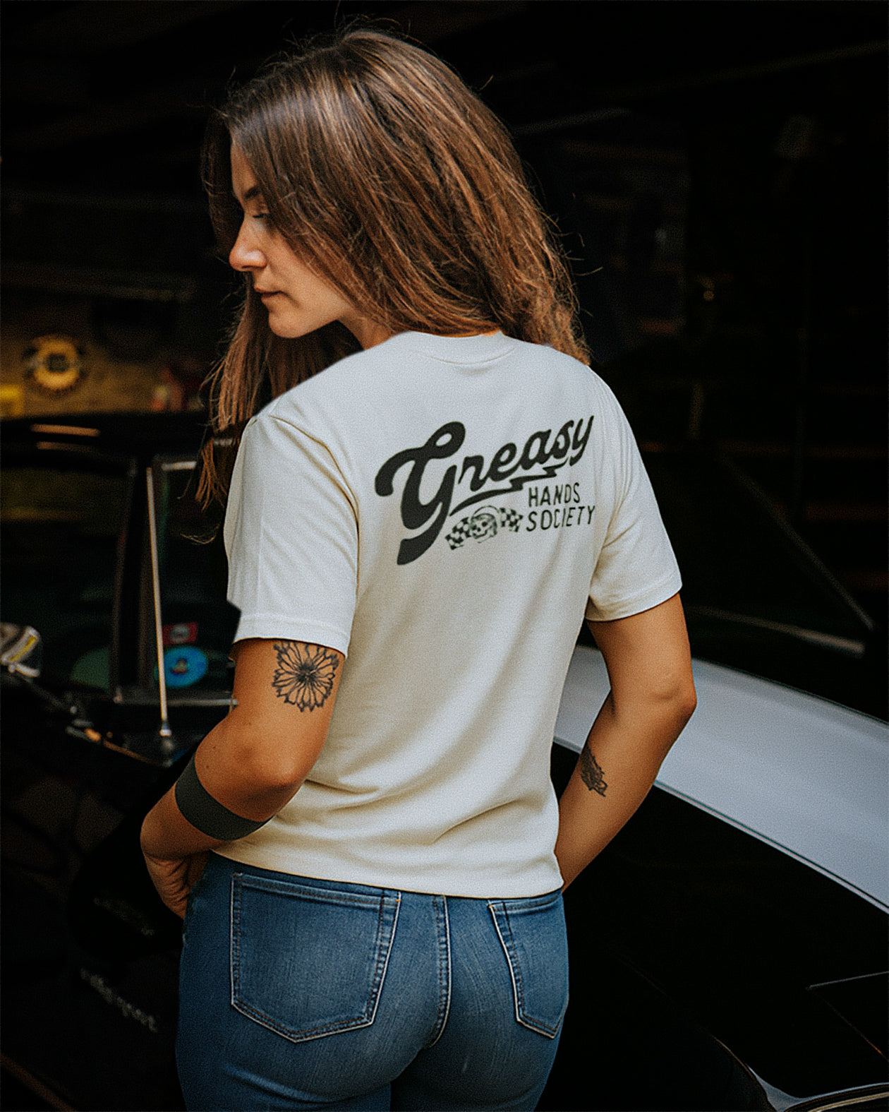 destination vintage white graphic tee for women - Woman wearing a white t-shirt with 'Greasy Hands Society' text, standing in a dark room.