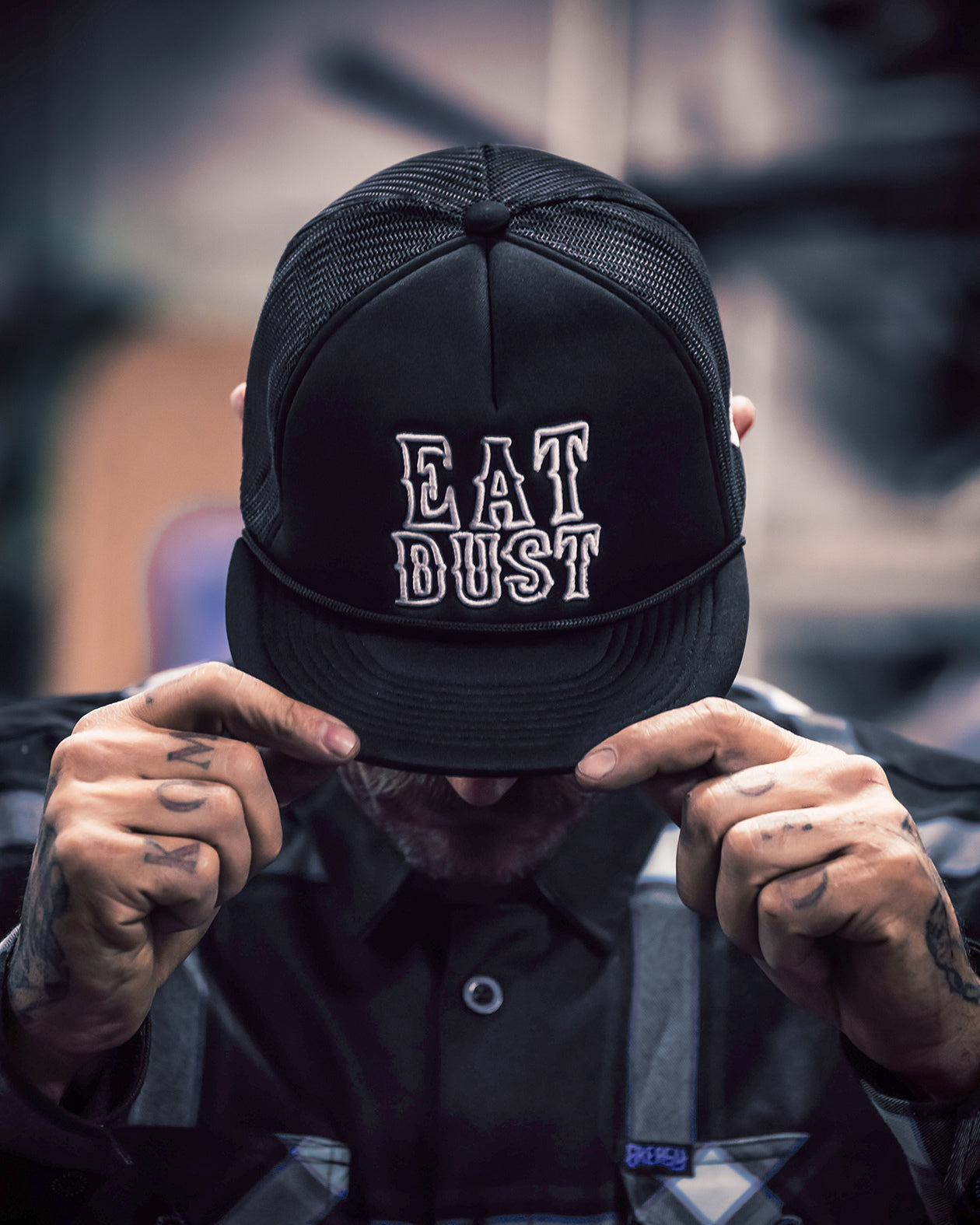 Person wearing a black cap with 'EAT DUST' text, holding it over their face.