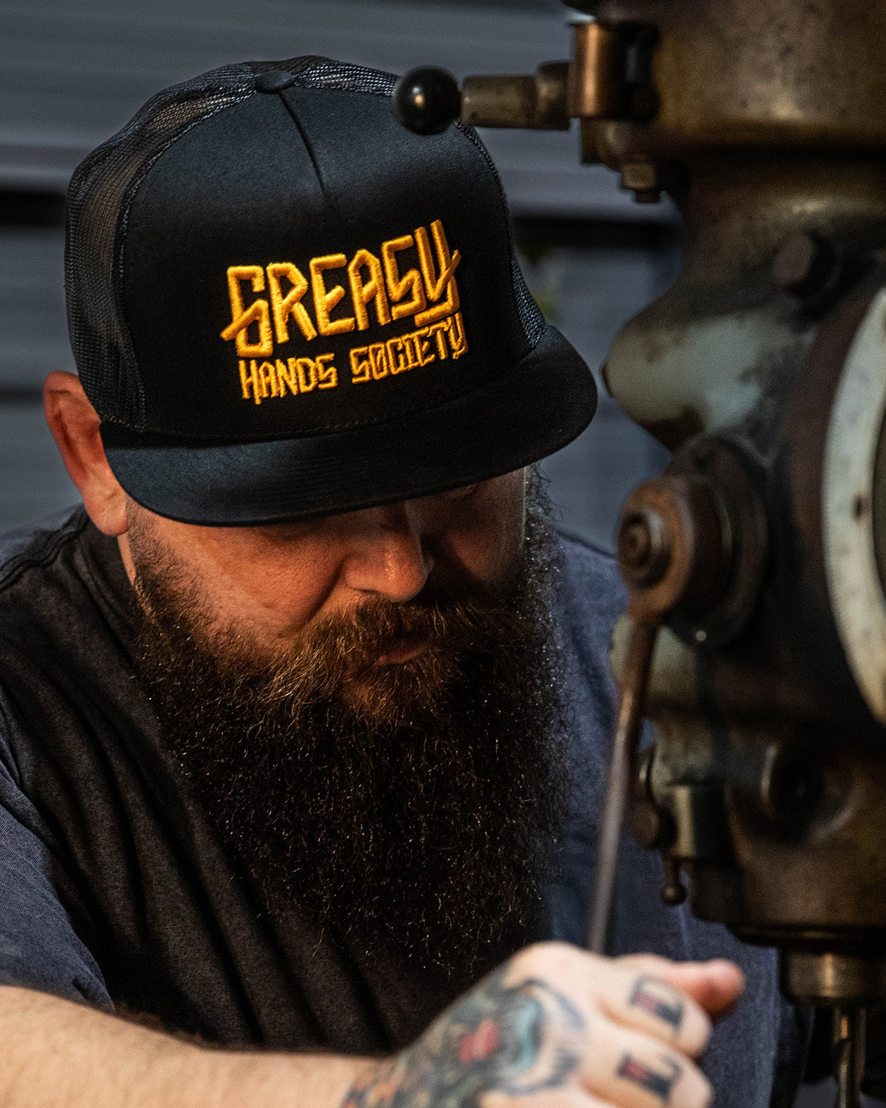 greasy hands society black hat with gold logo on a man working with his hands