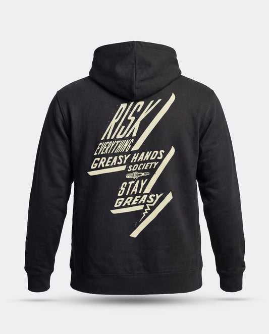 A black pullover hoodie shown from the back, featuring a large cream-colored graphic print with the text 'RISK EVERYTHING - GREASY HANDS SOCIETY - STAY GREASY' and diagonal lightning-bolt shapes, on a light gray background - Bolted Down Black Hoodie by Greasy Hands Society