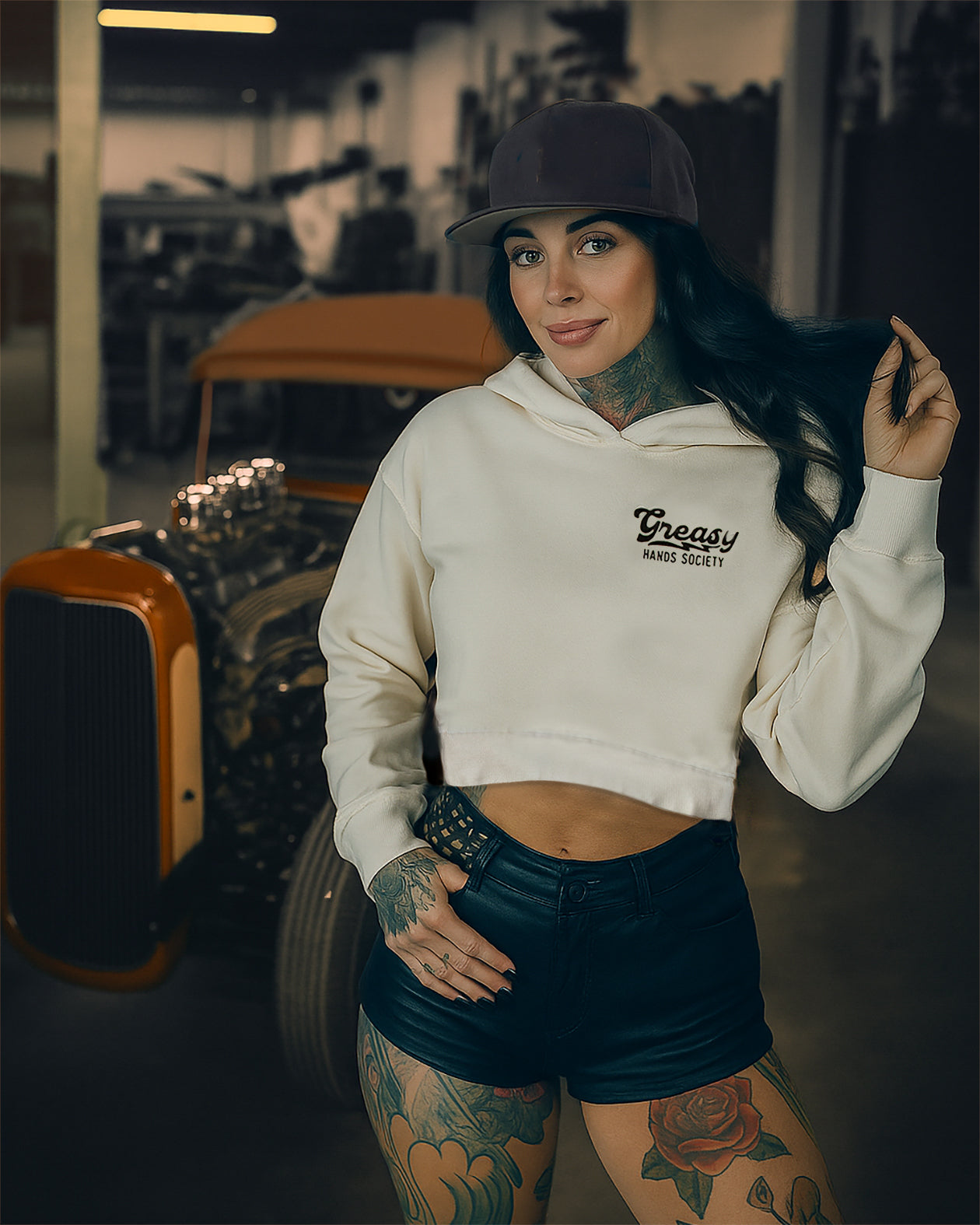 women's vintage white graphic crop top hoodie showing greasy hands society on the left chestwoman wearing a white hoodie with a logo and dark shorts in an indoor setting.