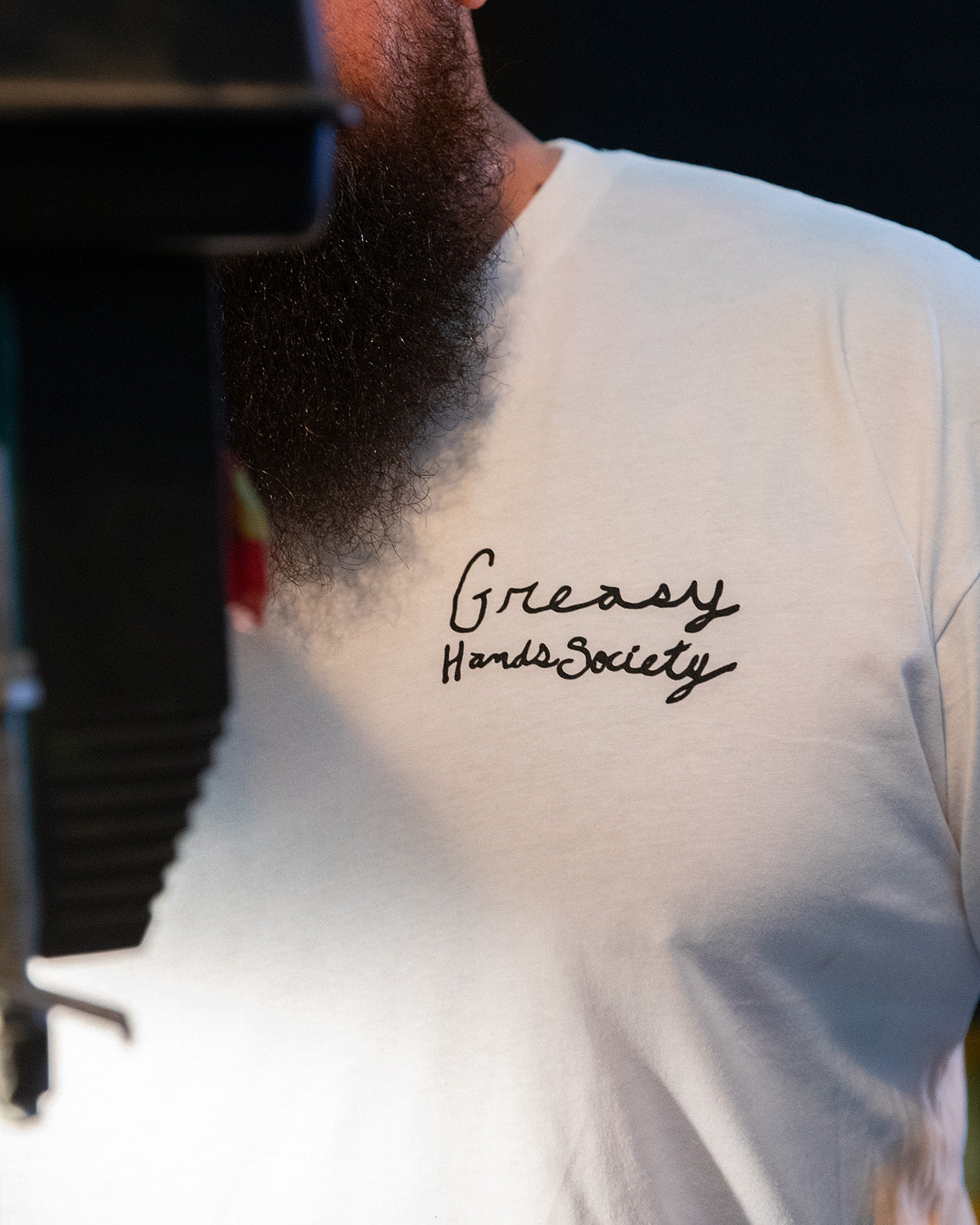 Person wearing a white t-shirt with 'Greasy Hands Society' text on the front left chest -n the break loose white graphic tee