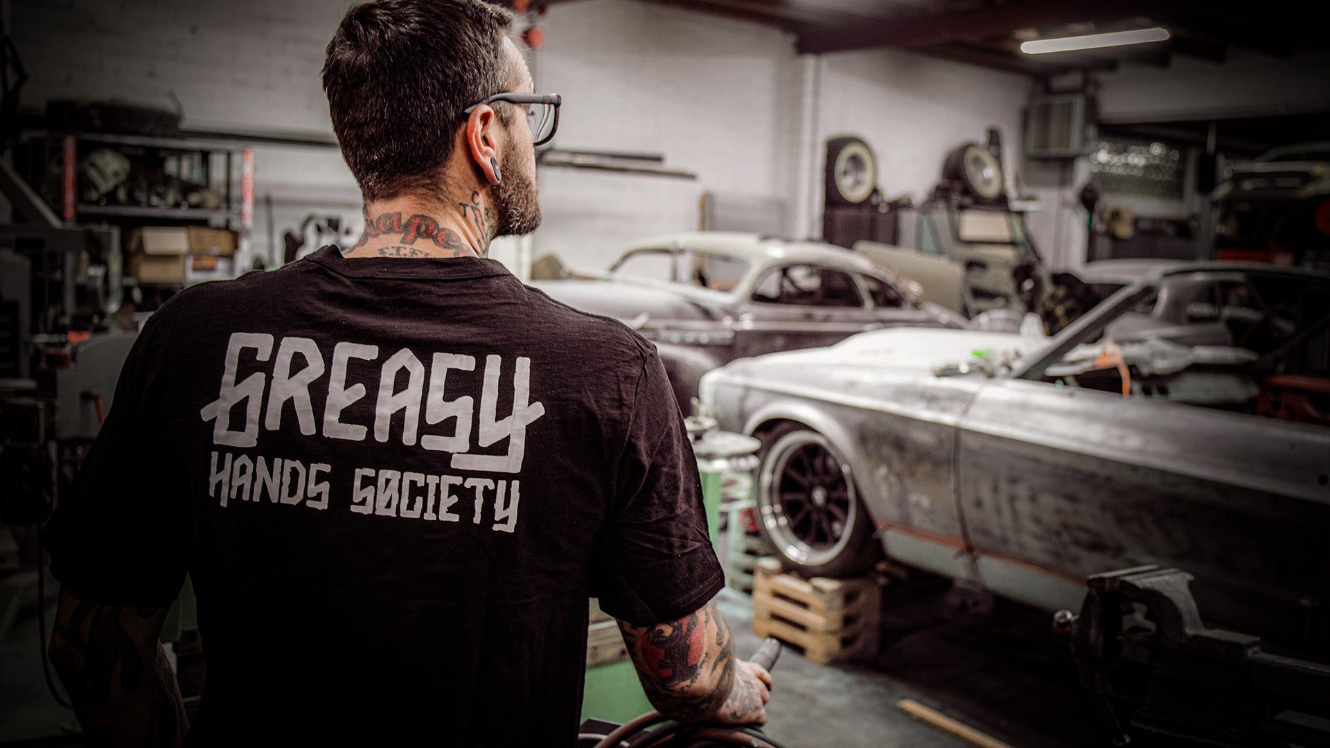 greasy hands society black logo t-shirt worn by a guy working in his car shop