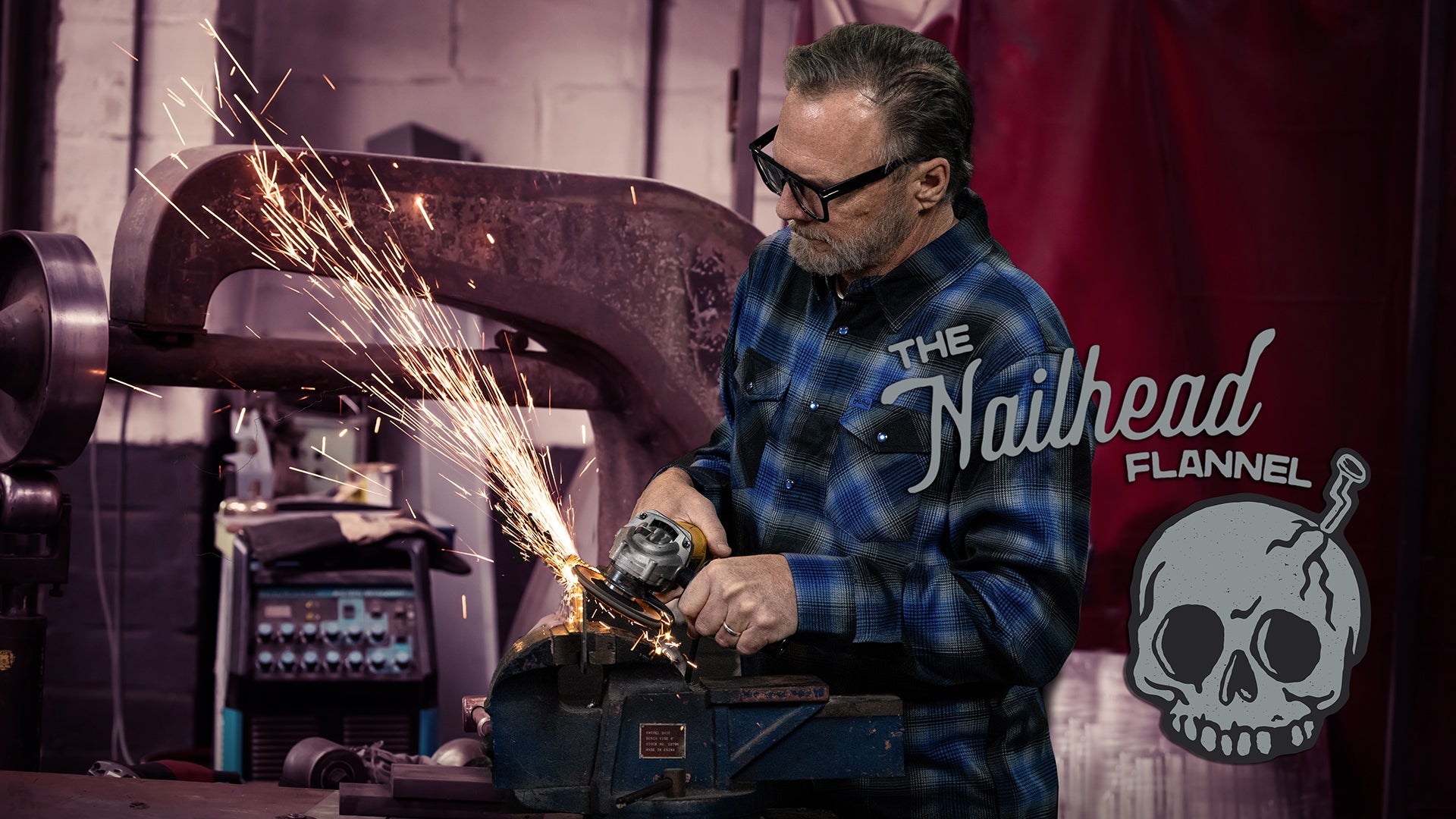 Man wearing a blue plaid shirt with 'The Nailhead Flannel' logo, working with sparks in a workshop.