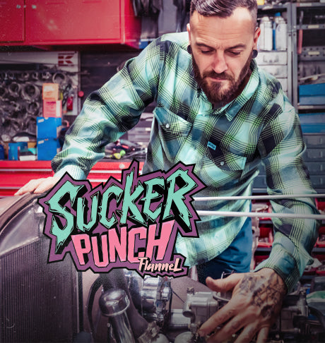 Man working on a car in a garage in a black green and blue flannel with 'Sucker Punch' logo overlay