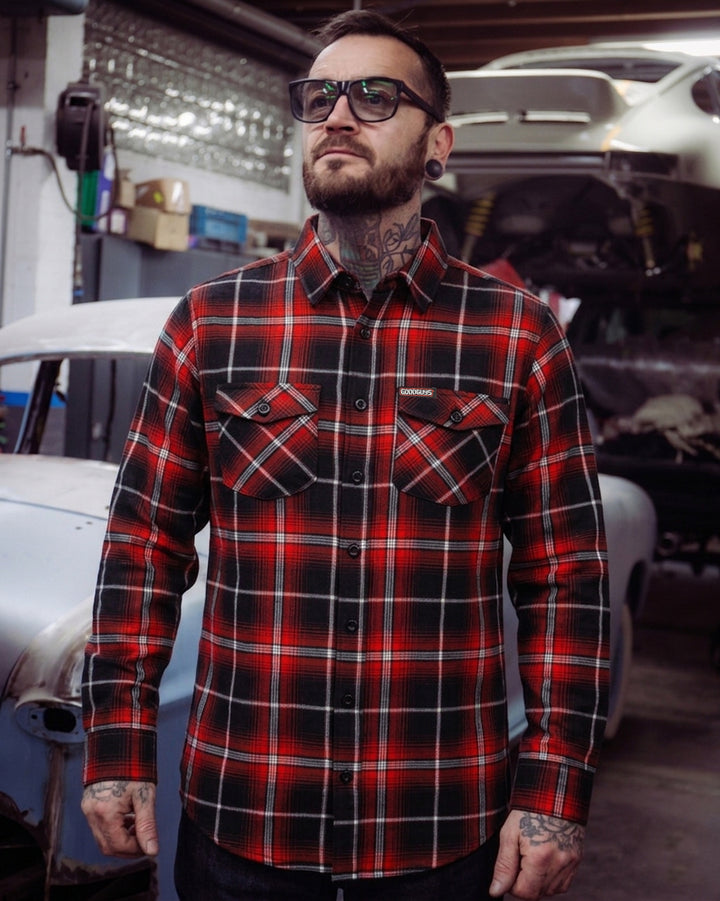 Man wearing a red and black plaid flannel shirt in a garage setting - The Detour Flannel by Greasy Hands Society