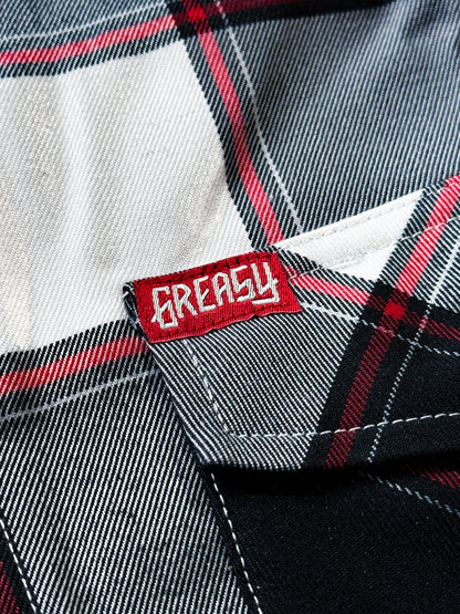 Close-up of a black, white and red plaid button-up flannel shirt fabric with a red embroidered patch label reading 'GREASY' in white text - Suicide Machine Flannel by Greasy Hands Society