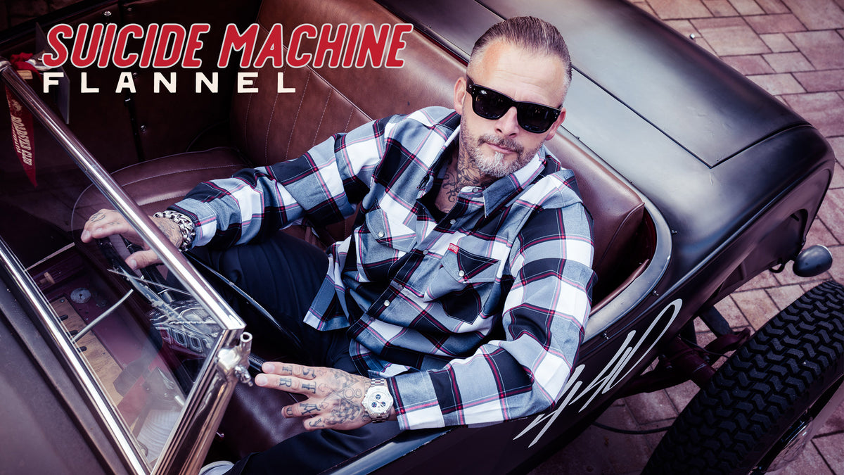 A man wearing a black and white buffalo plaid button-down flannel shirt and black sunglasses sits in a vintage black convertible car with brown leather seats - The Suicide Machine Flannel by Greasy Hands Society