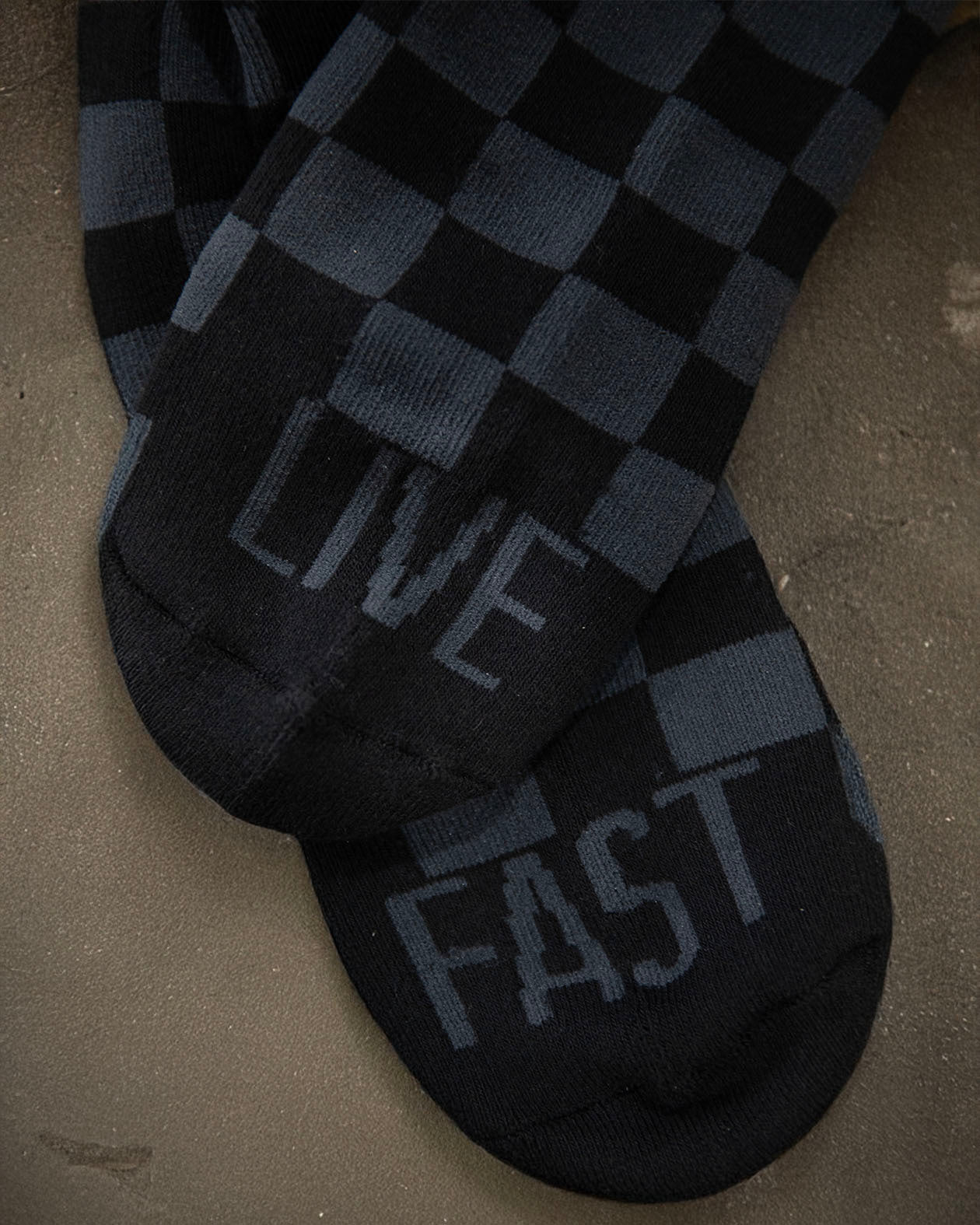 Black and gray checkered sock with 'Live Fast' text on a concrete surface