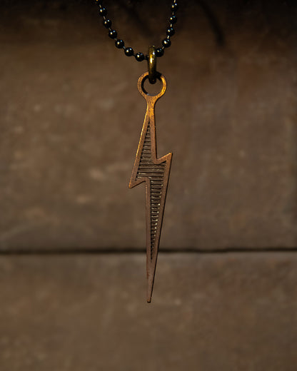 Bronze lightning bolt pendant on a dark chain against a brown background - LTNG Necklace by Greasy Hands Society