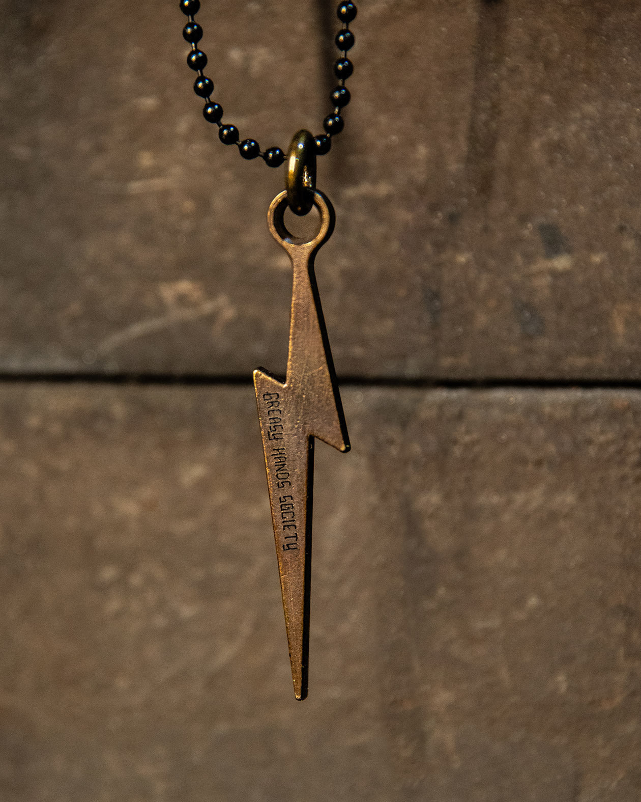 Bronze lightning bolt pendant on a black beaded necklace against a brown stone background