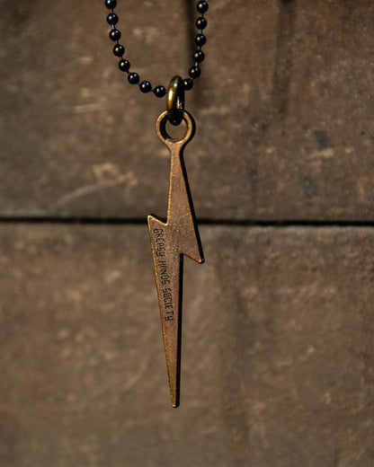 Bronze lightning bolt pendant on a black beaded necklace against a brown stone background