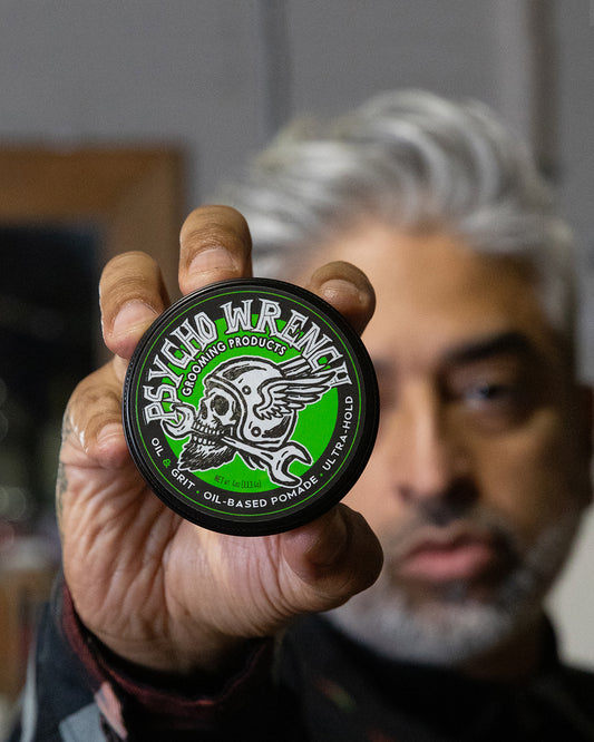 Person holding a container of 'Psycho Wrench' oil based pomade with a blurred background