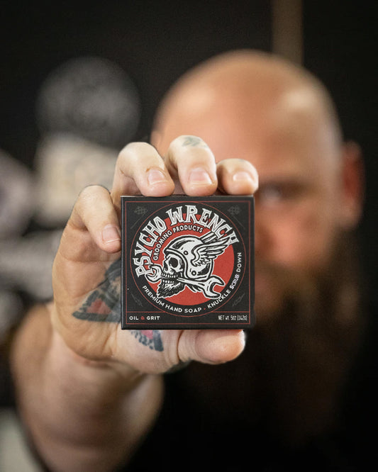 Man holding a box of soap called 'Psycho Wrench knuckle scrub down bar soap' against a dark background