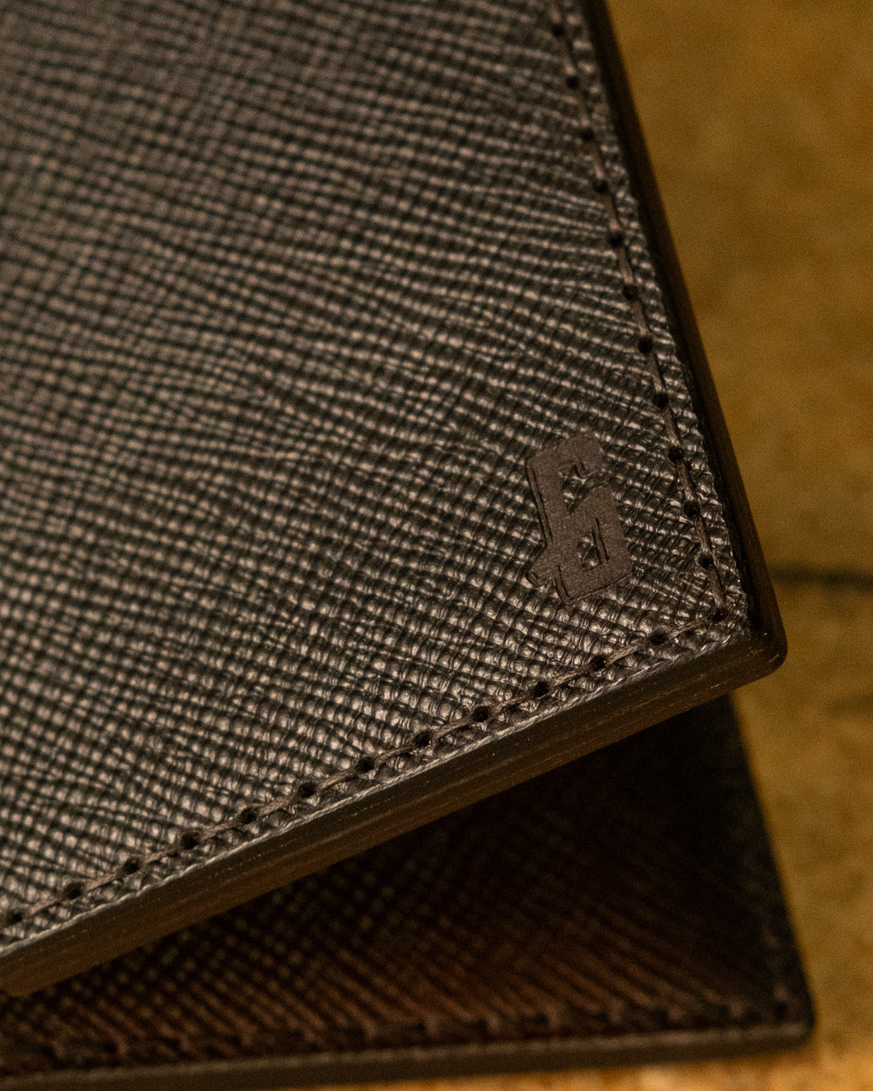 Close-up of a textured brown wallet with a brand logo on a blurred background