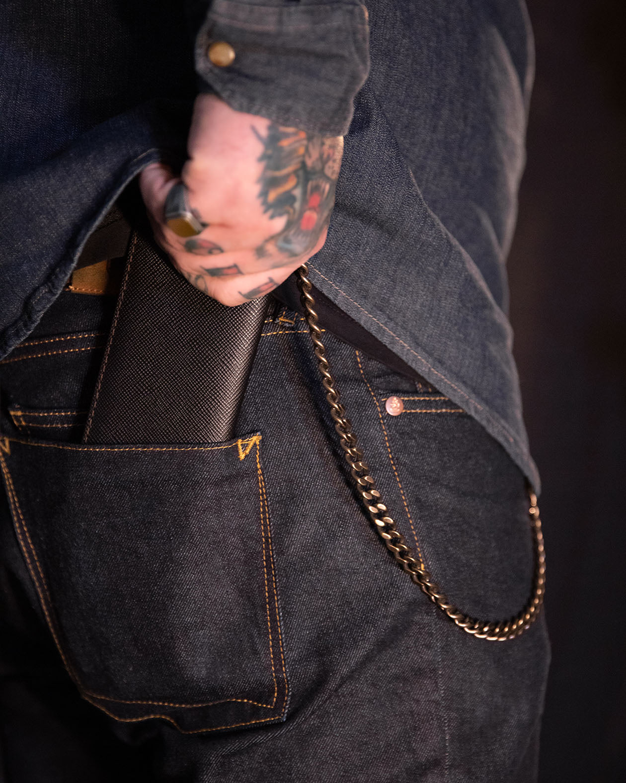 Person wearing dark denim jeans with a gold chain detail attached to a wallet, holding a black wallet.