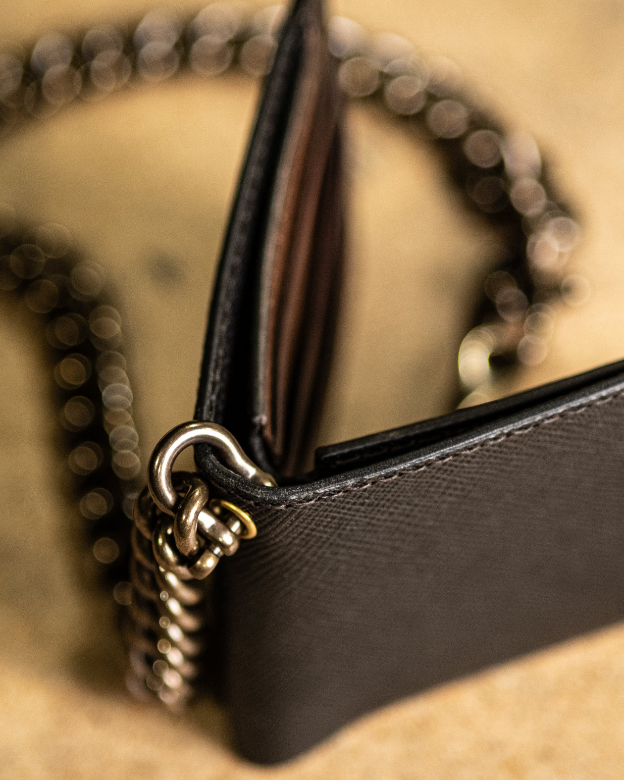 Close-up of a brown leather handbag with gold chain strap on a beige background