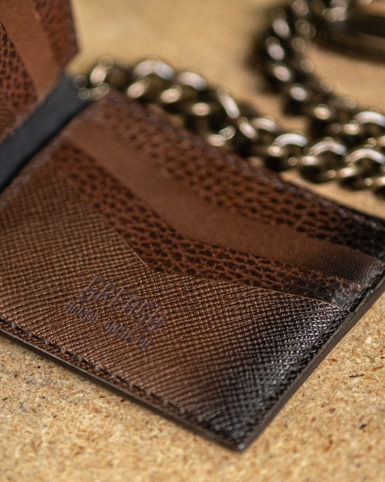 Close-up of a brown textured wallet with a chain on a beige surface