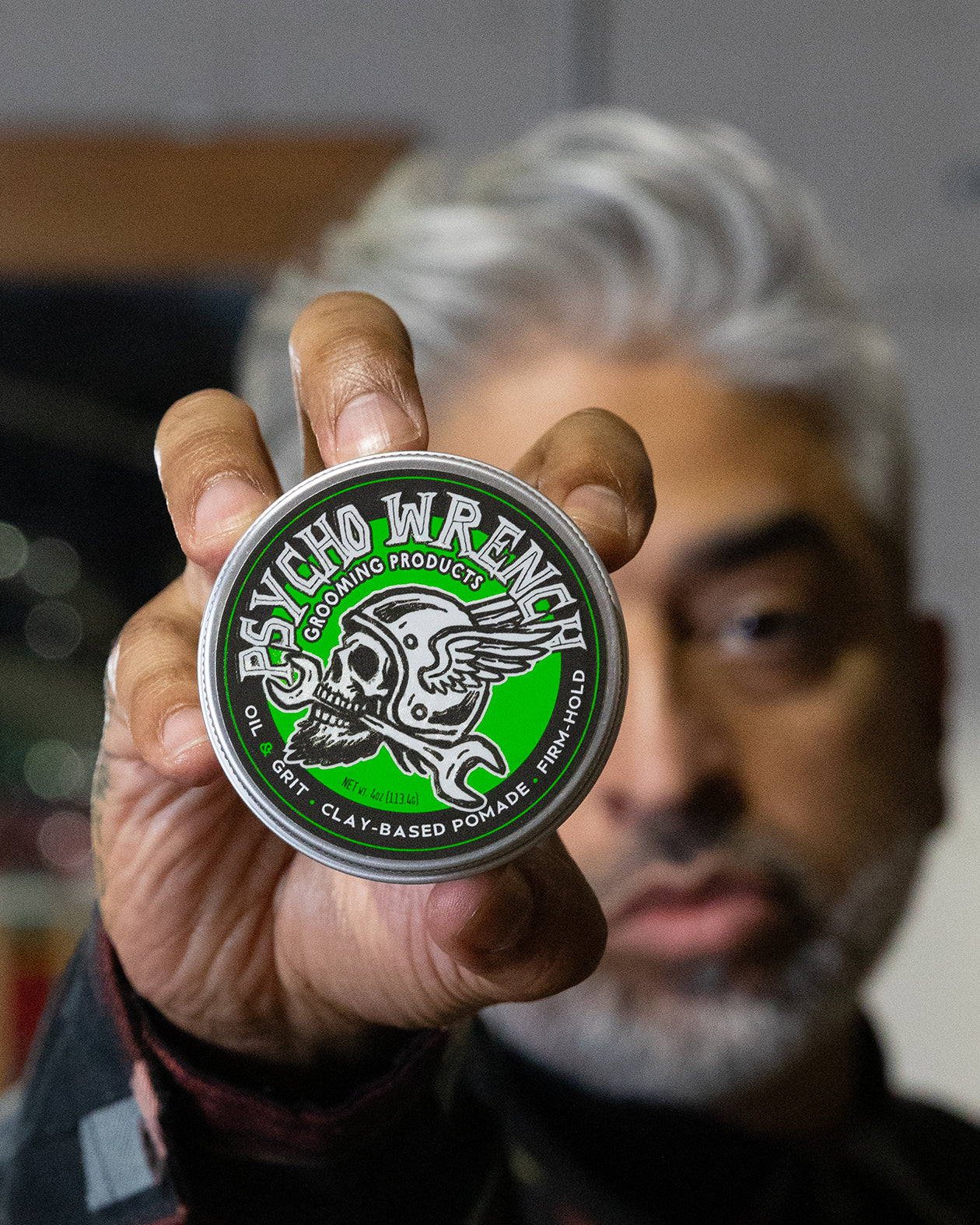 Person holding a container of Psycho Wrench clay-based pomade with a blurred background