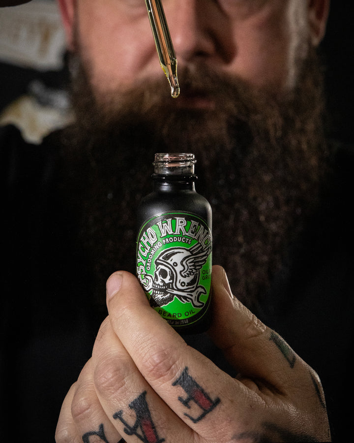 Person holding a bottle labeled 'Psych Wrench gooming products beard oil' with a dropper close to the bottle.