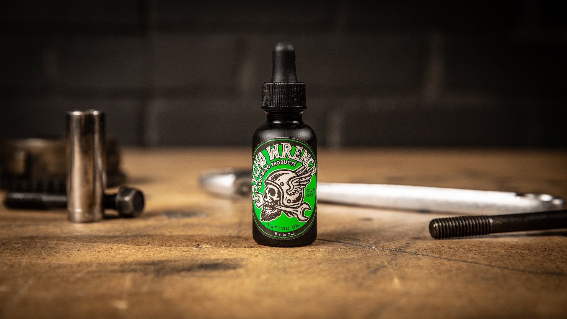 Bottle of 'Green' psycho wrench tattoo oil - scent oil & grit on a wooden surface with tools in the background