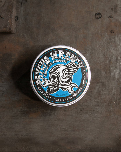 Metallic tin labeled 'Psycho Wrench Grooming Products' on a textured surface - Cold Start Clay-based pomade from Psycho Wrench by Greasy Hands Society