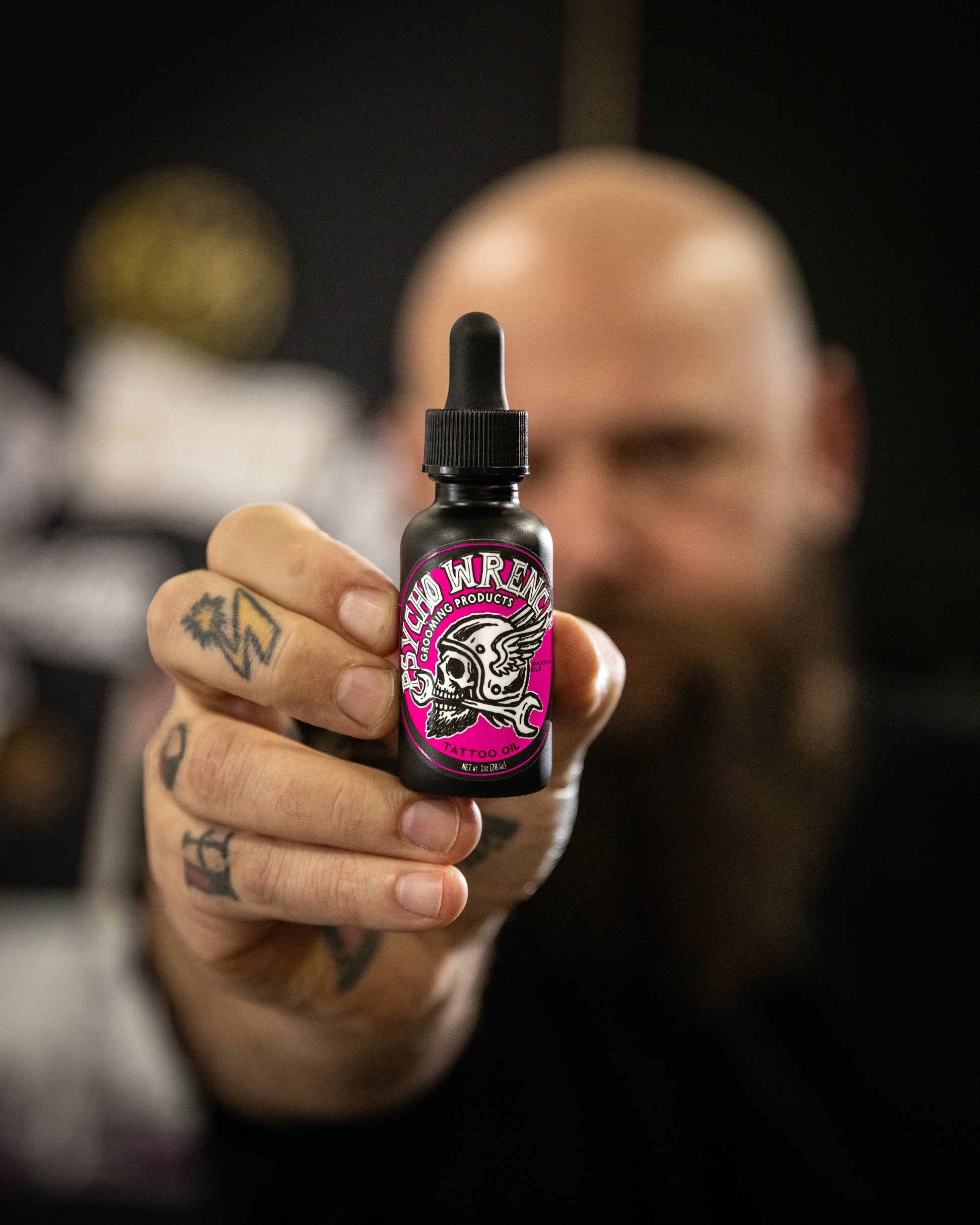 Person holding a bottle of 'smooth idle tattoo oil' product with a blurred background