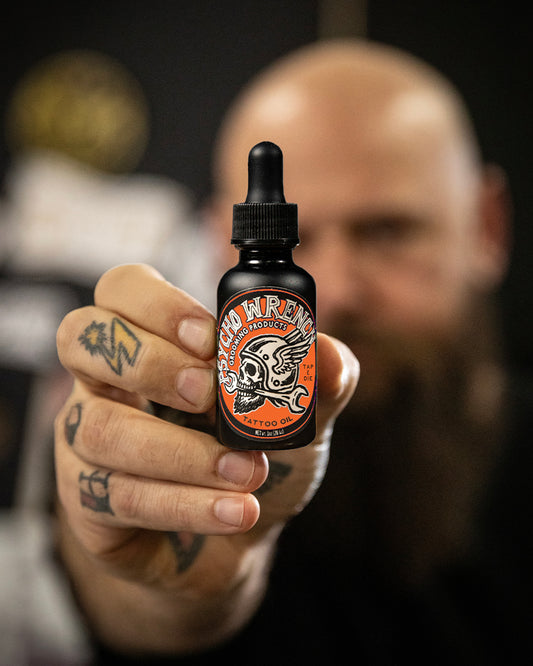 Person holding a bottle of 'Psycho Wrench' beard oil with a blurred background - Psycho Wrench Tap & Die Tattoo Oil by Greasy Hands Society