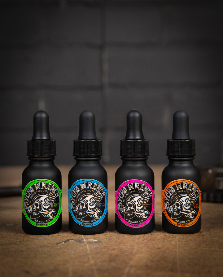 Four black bottles with colorful labels on a wooden surface and dark background - Beard Oil Variety 4-pack by Greasy Hands Society
