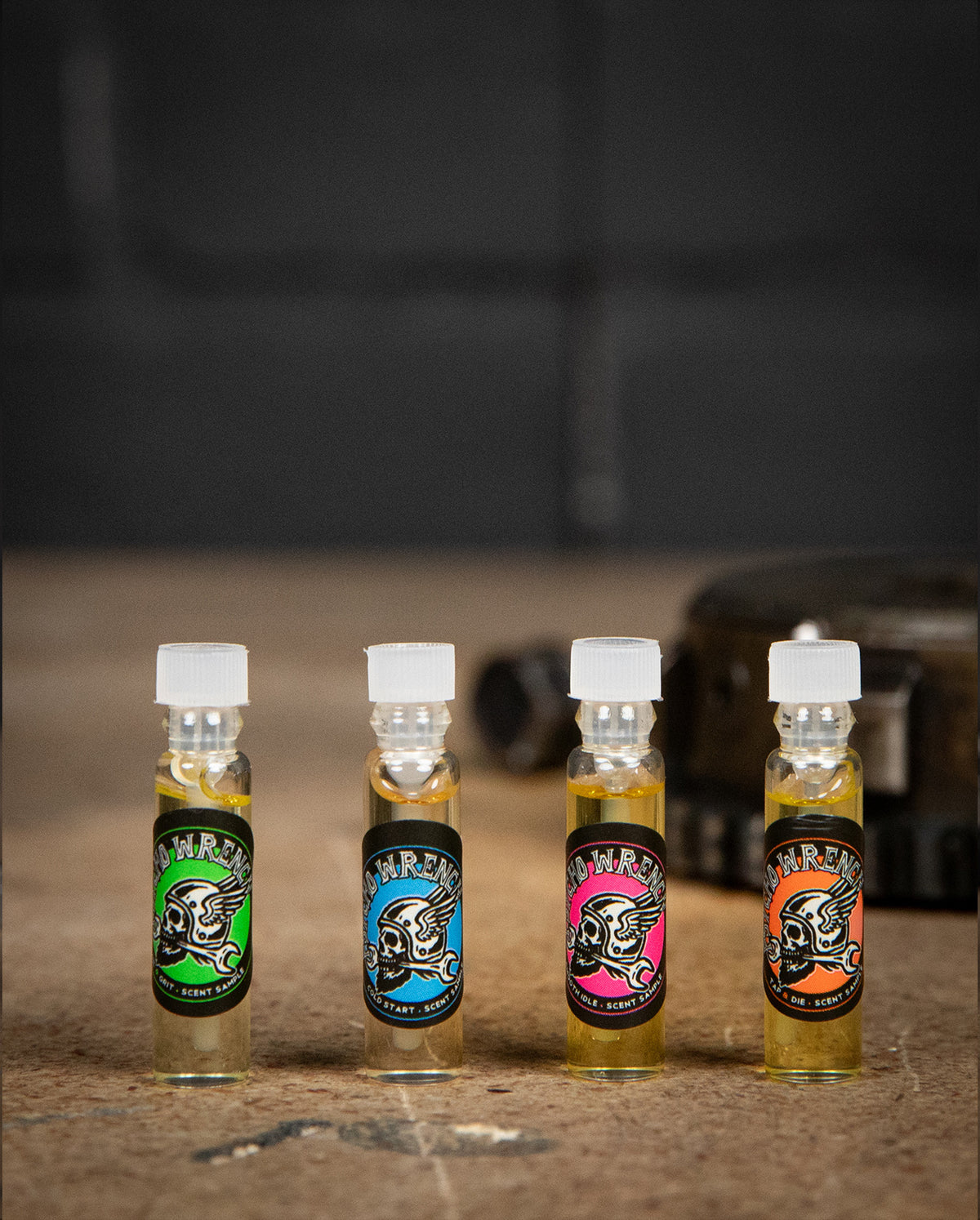 Four small bottles with colorful labels on a textured surface - body oil sample by greasy hands society - Psycho Wrench Scent Sampler by Greasy Hands Society