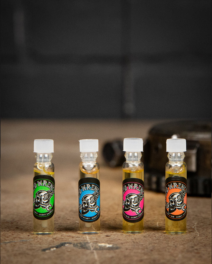 Four small bottles with colorful labels on a textured surface - body oil sample by greasy hands society - Psycho Wrench Scent Sampler by Greasy Hands Society