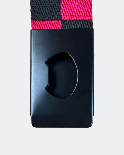A close-up of a black belt buckle with a matching black and bright pink checkered woven strap, shown against a light gray background.