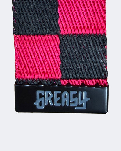 A close-up of a woven belt featuring a pink and black checkered pattern, with a black buckle engraved with the word 'GREASY' in stylized lettering - Pink Noise Belt by Greasy Hands Society