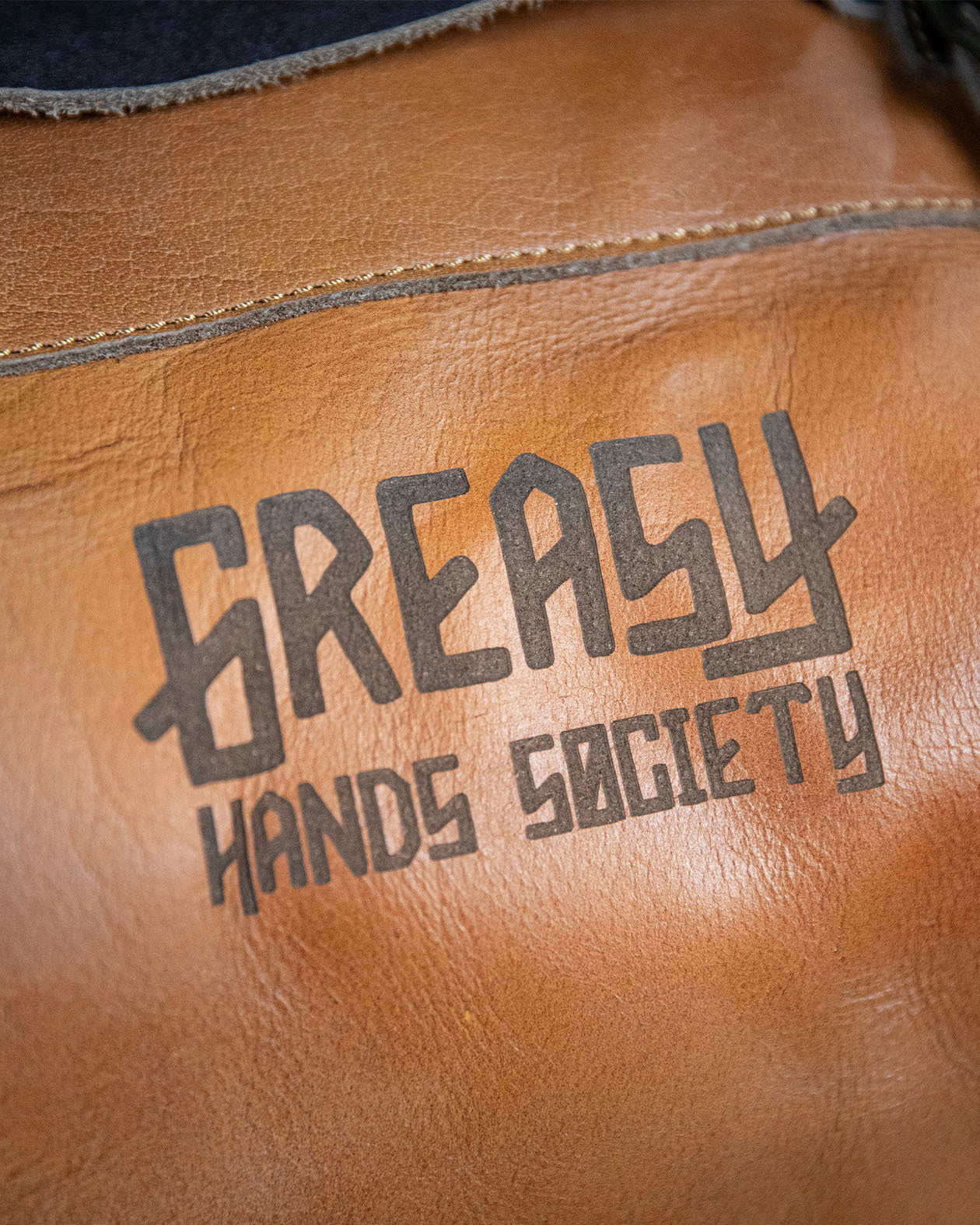 detail of the greasy hands society logo on the brown leather duffel bag