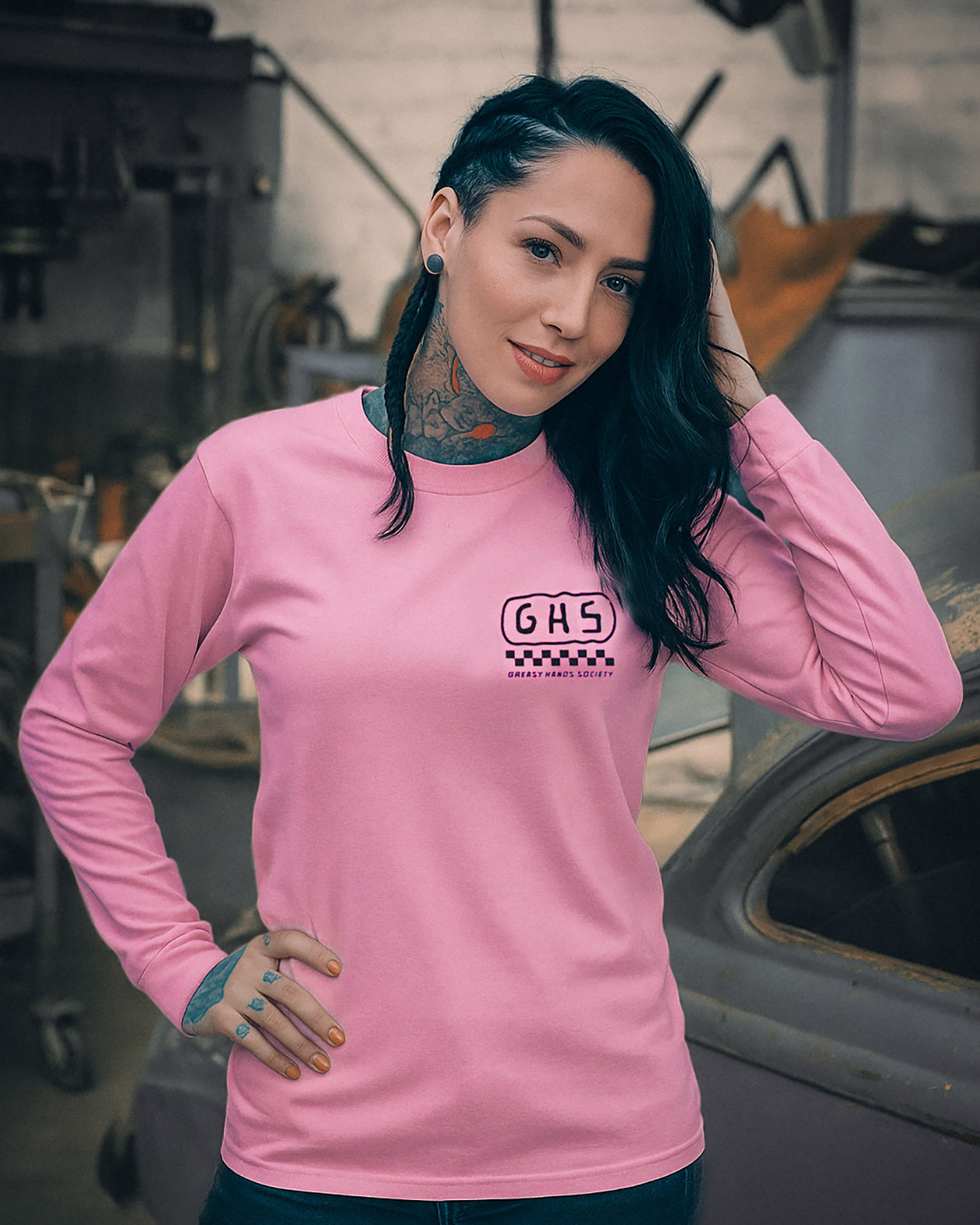 Woman wearing a pink long-sleeve shirt with a logo, standing in a garage. GHS-Engineered pink long sleeve shirt