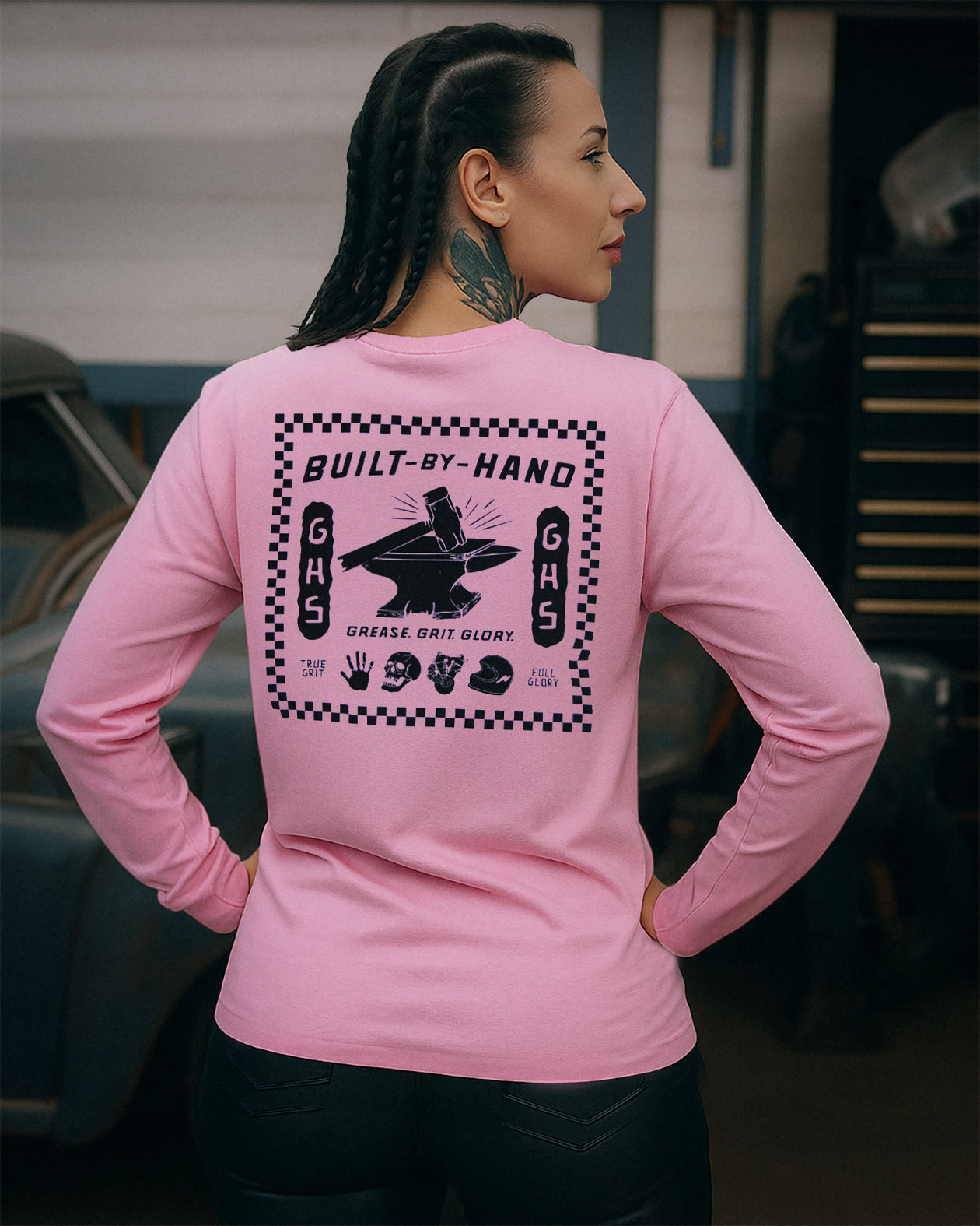 woman wearing a pink long-sleeve shirt with a graphic design on the back, standing in a garage.