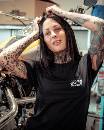 Woman wearing a black t-shirt with the greasy hands society logo standing in a workshop.