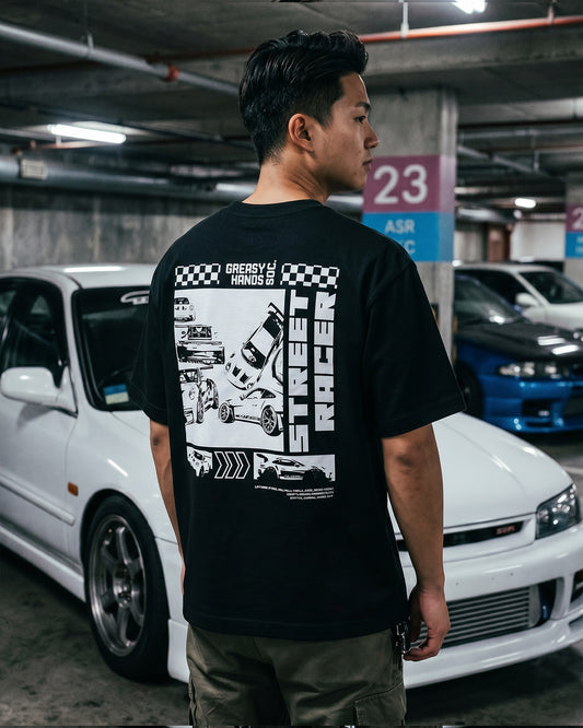 Person wearing a black t-shirt with a JDM street racing graphic design in a parking garage - Street Racer Men's Graphic Tee by Greasy Hands Society