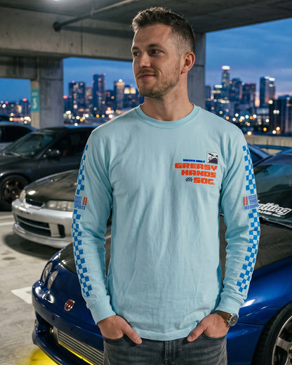 Man wearing a light blue long-sleeve shirt with JDM graphics and text, standing in an urban setting with cars and city lights - GHS MOTORSPORTS long-sleeve graphic tee by greasy hands society