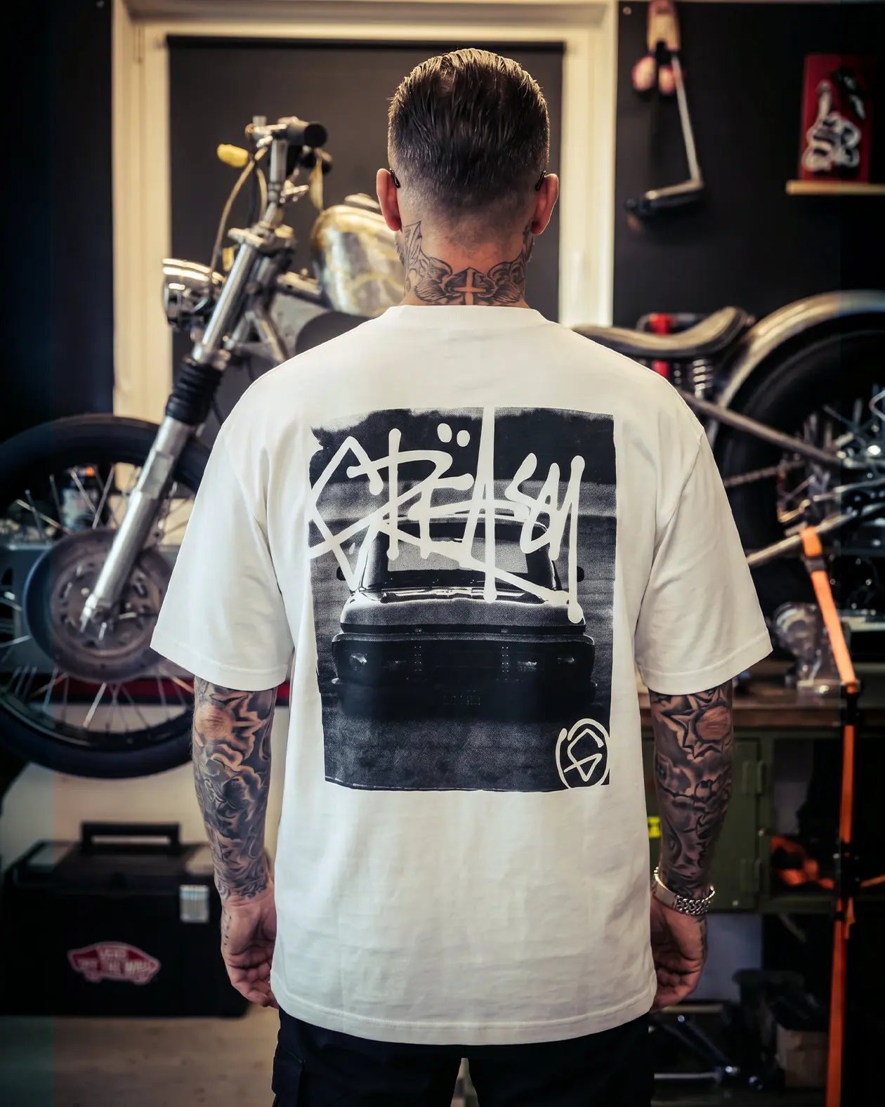 Person wearing a white t-shirt with black graphic design in a motorcycle workshop - Slam'd White Heavyweight graphic Tee by Greasy Hands Society