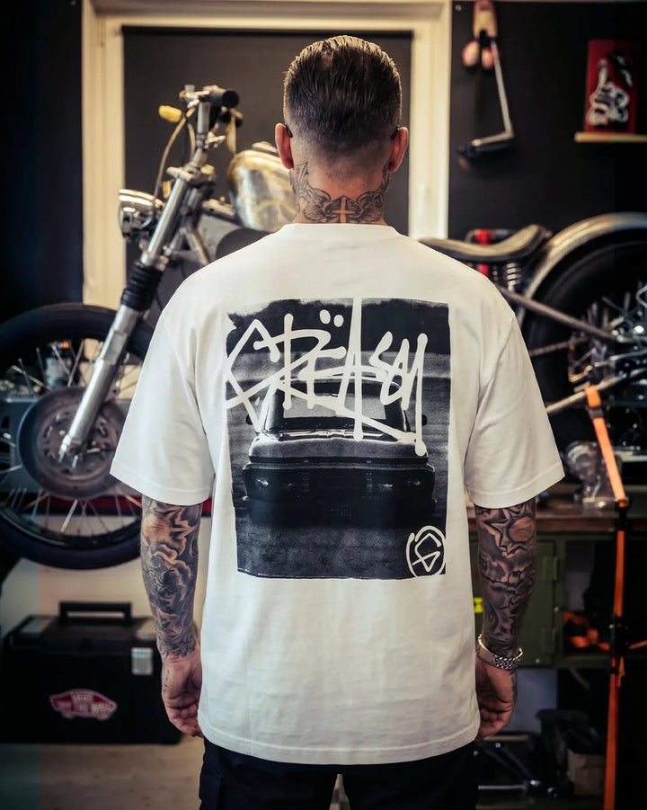 Person wearing a white t-shirt with black graphic design in a motorcycle workshop - Slam'd White Heavyweight graphic Tee by Greasy Hands Society
