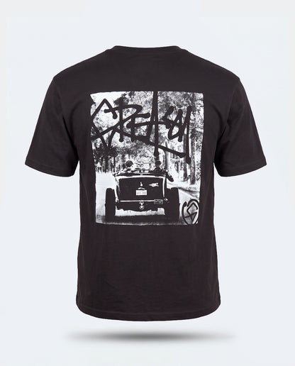 A black short-sleeve t-shirt shown from the back, featuring a large white graphic print of a vintage hot rod car in a forest with graffiti-style lettering - Detroit Steel Graphic Tee by Greasy Hands Society