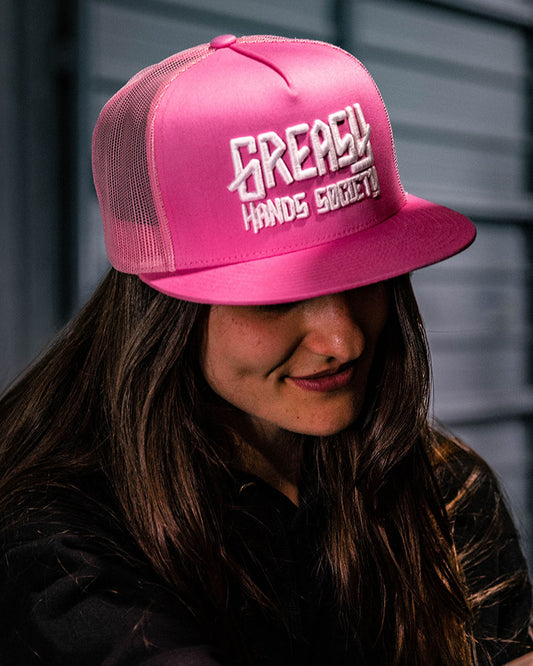 A person wearing a pink 'GREASY HANDS SOCIETY' logo cap with a white brim. The cap has a flat bill and an adjustable snapback closure - GHS Pink & White Logo Hat by Greasy Hands Society
