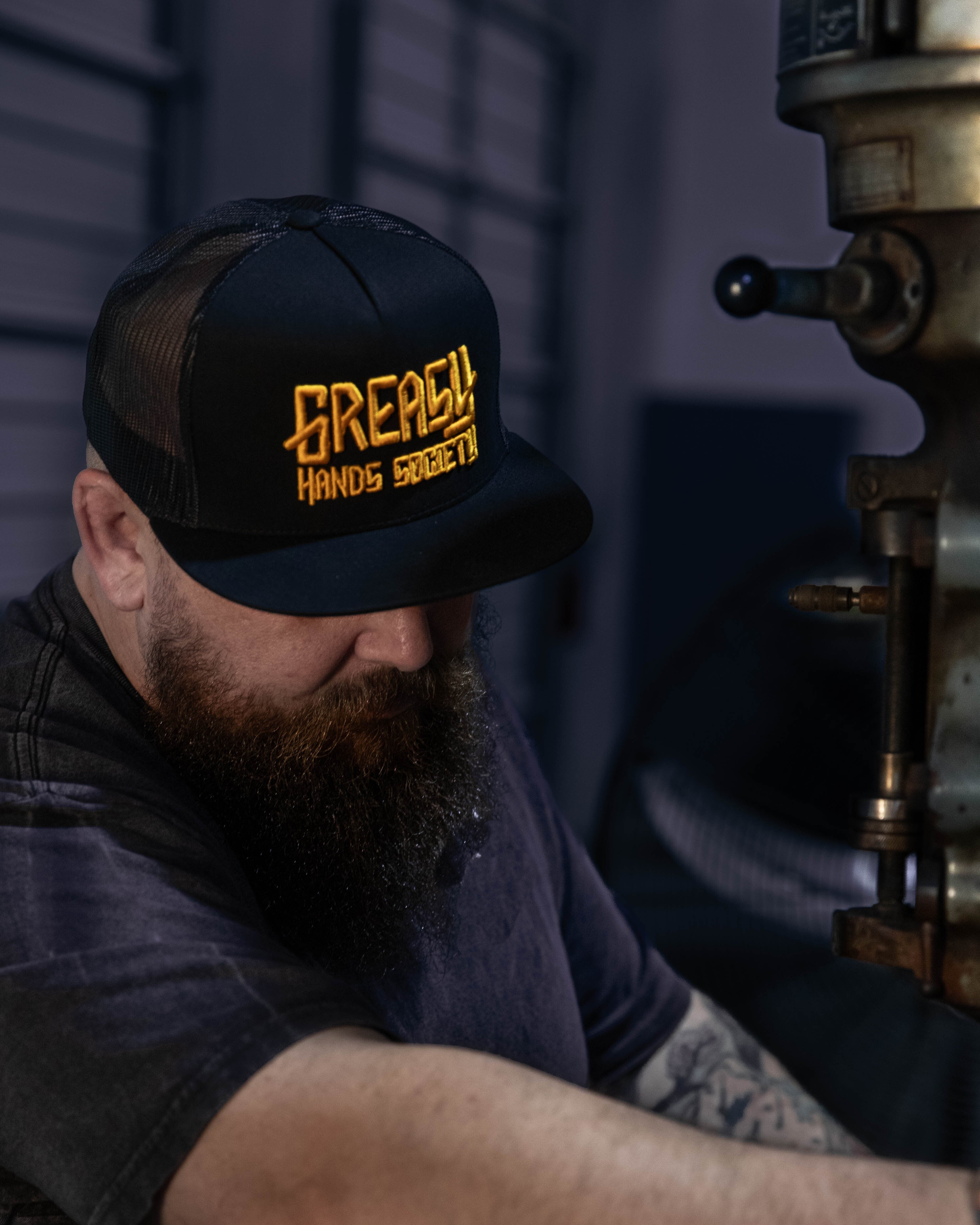 greasy hands society black hat with gold logo on a man working with his hands