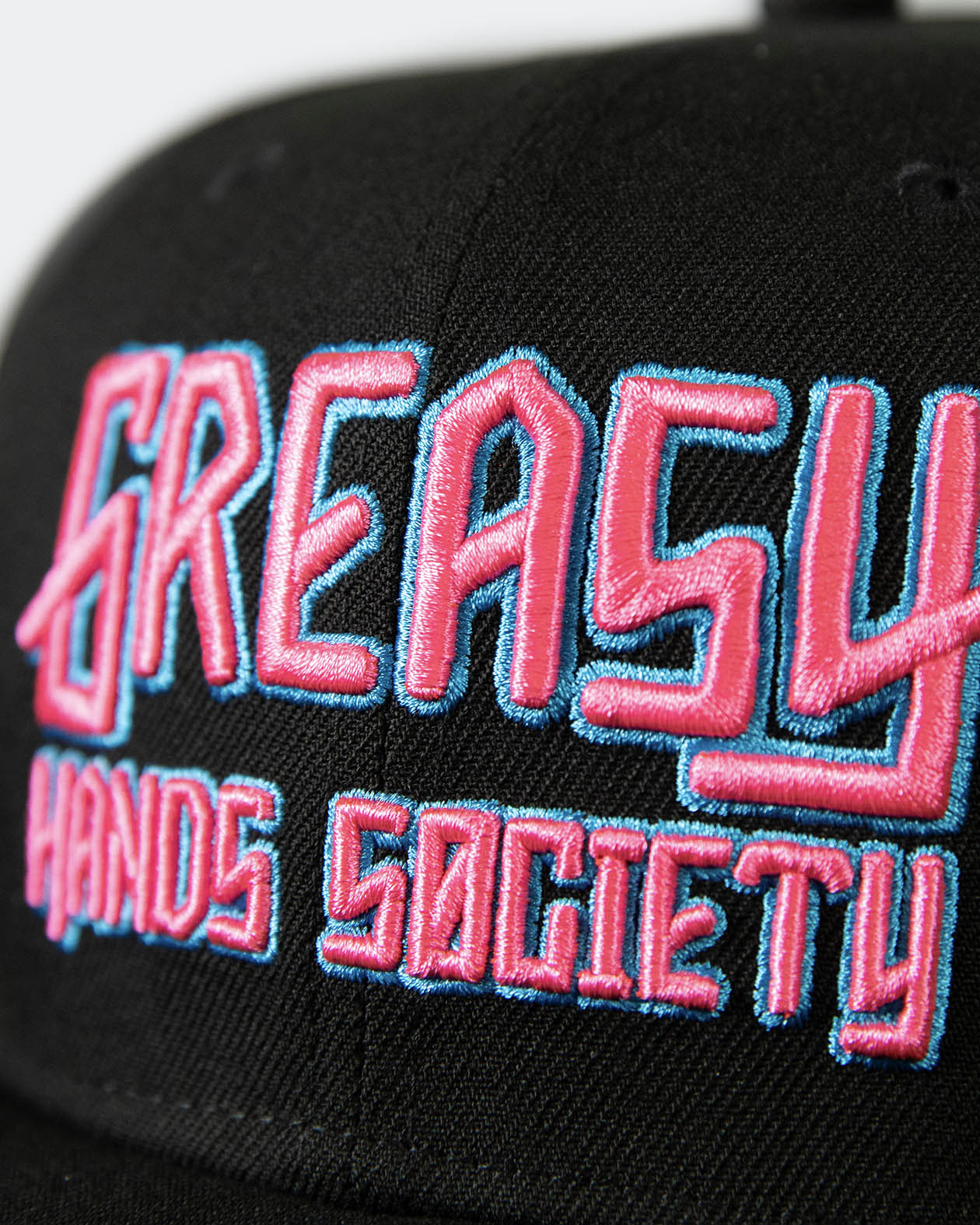 detail shot of a black cap with pink and blue greasy hands society logo on the front - showing the stitching