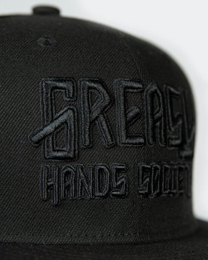 detail shot of a black cap with black greasy hands society logo on the front - showing the stitching